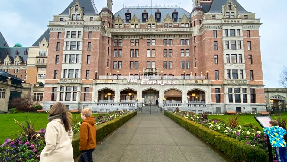 Bâtiment de l'hôtel Empress vu de la rue avec deux piétons passant devant et un adolescent lisant un panneau de pelouse au premier plan