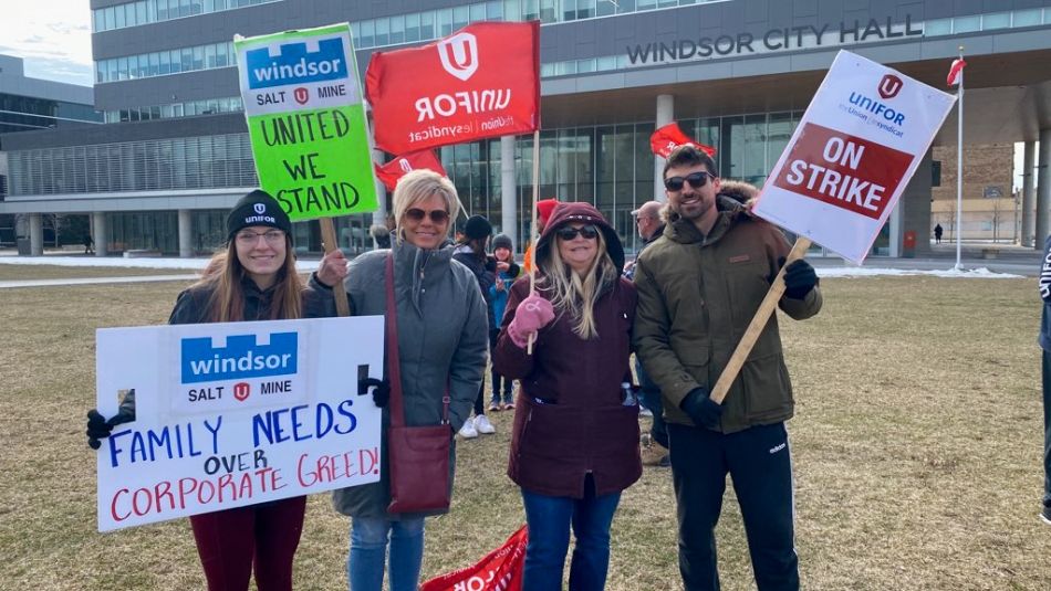 “Four people posing outside Windsor City Hall holding signs and On Strike placards”