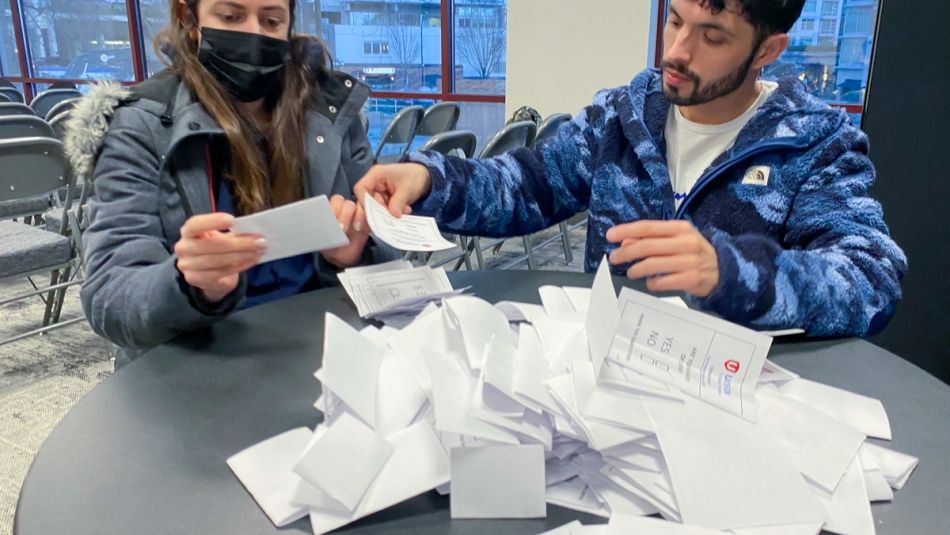 Two people sitted and counting ballots in a pile on a table. 