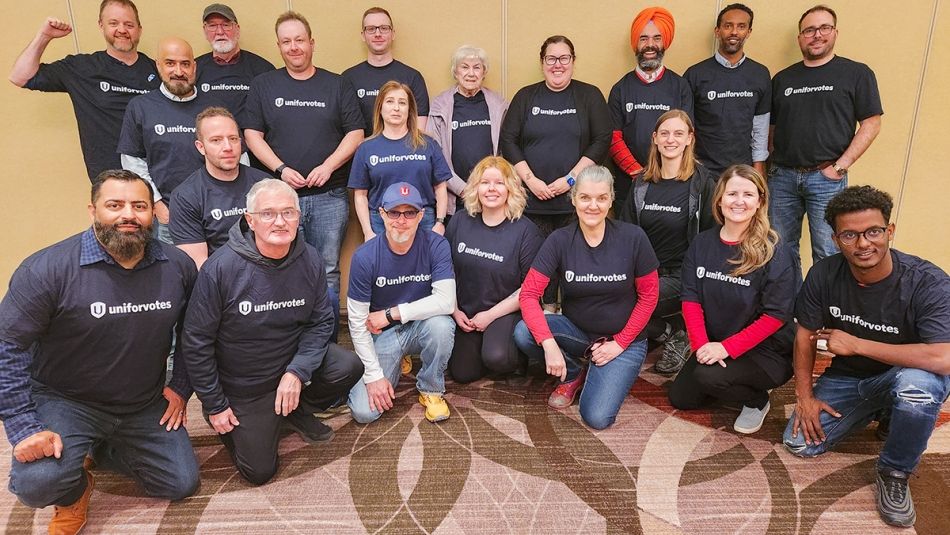 « Un groupe de 20 personnes portant des t-shirts avec la mention Unifor votes, certains agenouillées, d’autres debout. »