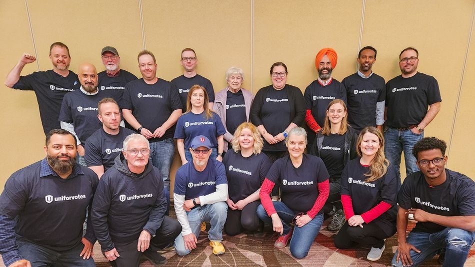 Groupe d'organisateurs membres d'Unifor portant des t-shirts noirs d'UniforVotes posant pour une photo, une rangée debout, une rangée devant à genoux.