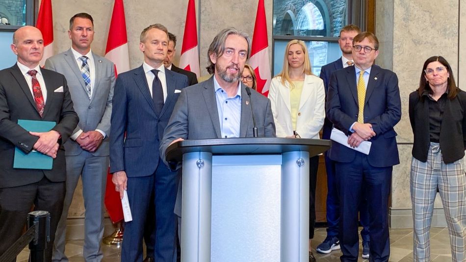 Gavin McGarrigle at the Sustainable Jobs Act press conference. Gavin McGarrigle speaks from a podium with several people behind him and four Canadian flags.