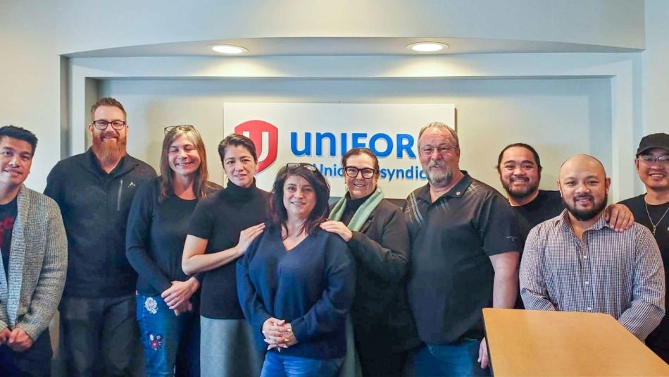 Ten people lined up for a photo in an office in front of Unifor signage.