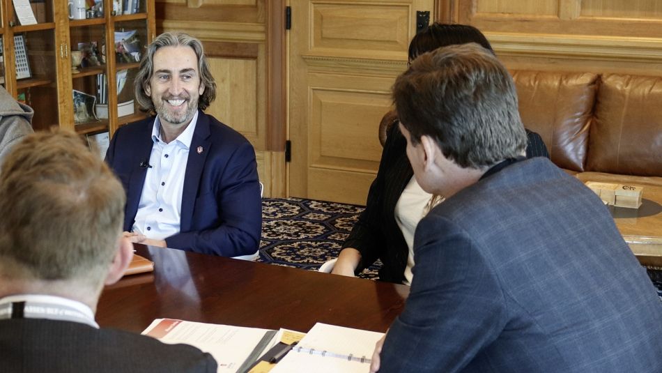 Gavin McGarrigle assis à une table de réunion, souriant aux autres participants.