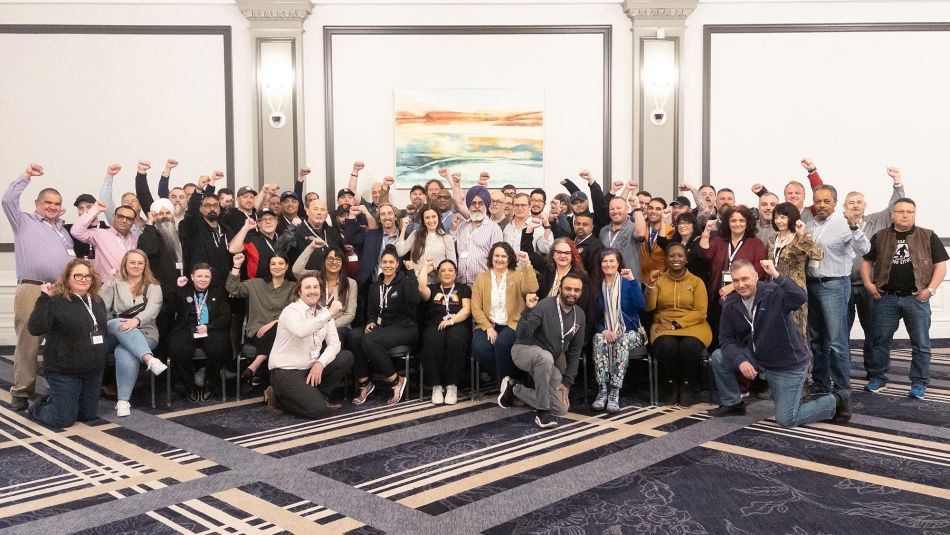 Un grand groupe de membres d'Unifor pose pour une photo dans la salle de bal, le poing droit en l'air.