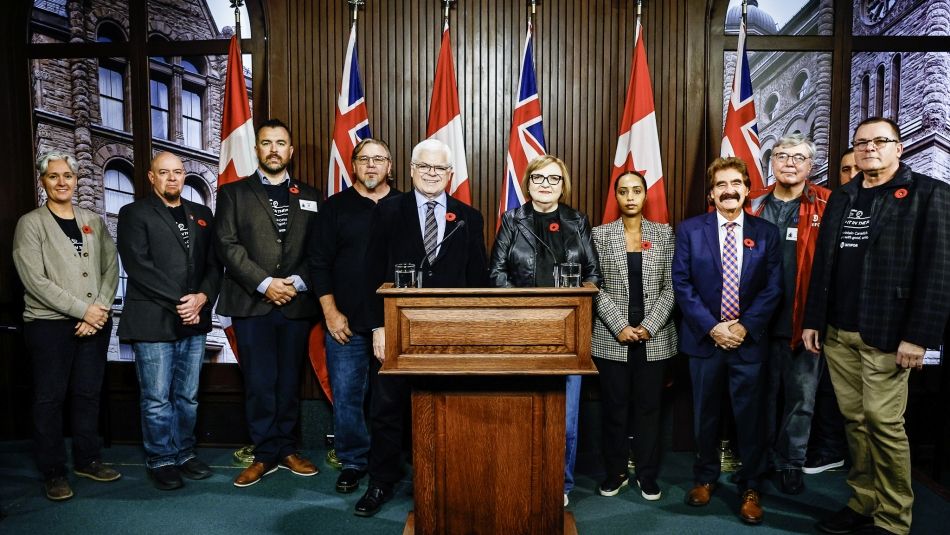 La présidente nationale d'Unifor, Lana Payne, la directrice régionale d'Unifor Ontario, Samia Hashi, et les membres du Conseil de l'énergie d'Unifor posent avec les députés provinciaux de l'ONDP, Peter Tabuns et Wayne Gates, lors de la conférence de presse de lancement de la campagne "Keep it in the Pipe" (Gardez-le dans le tuyau). Des personnes se postent pour une photo à l'intérieur devant les drapeaux du Canada et de l'Ontario, avec un podium en bois au premier plan.