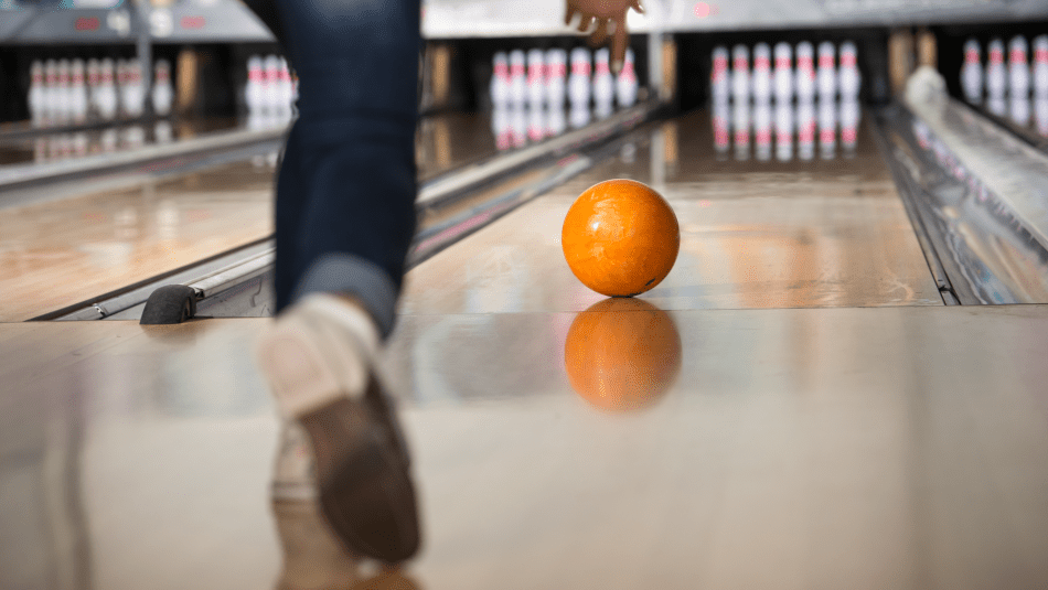 an orange bowling ball rolling down the lane toward the pegs