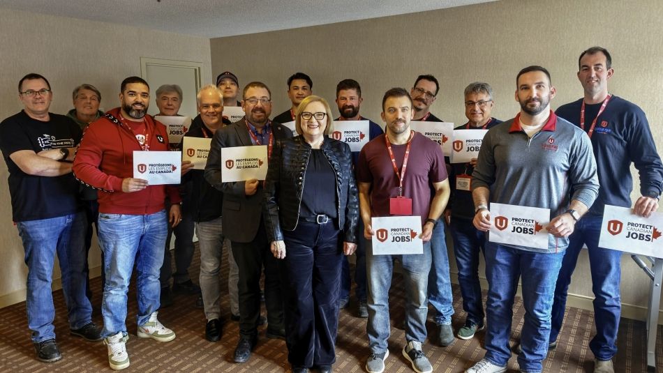 A group of workers standing with Lana Payne holding signs saying "Protect Canadian Jobs".