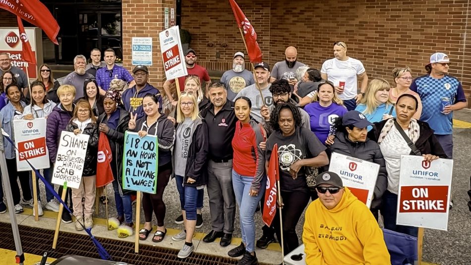 A group of approximately 40 workers pose for a photo with Unifor flags and On Strike 