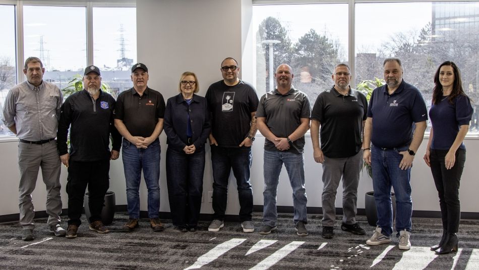 Nine people standing and posing for a group shot near windows.