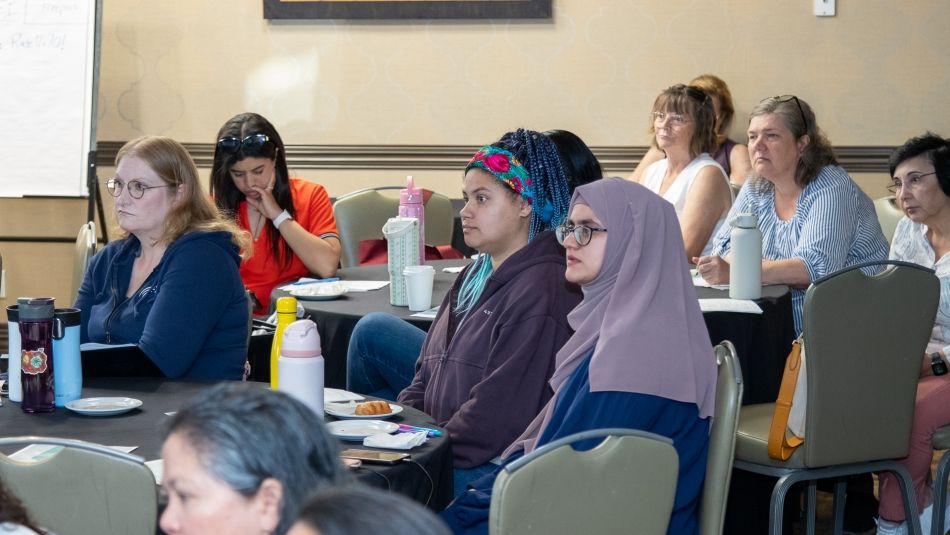 Several people seated about round tables listening to a presentation.