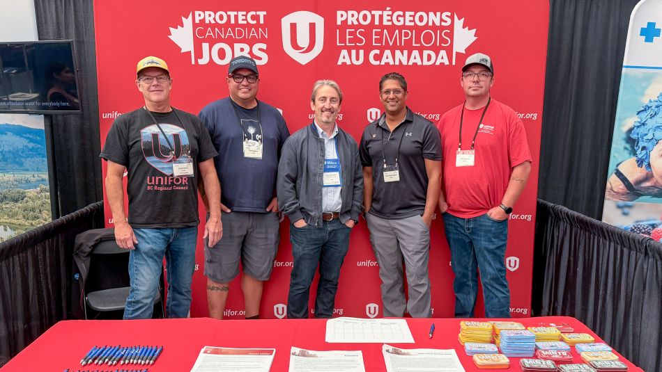 Five men standing in front of a backdrop reading 'Protect Canadian Jobs' with Unifor logos. A table is in the foreground with papers and pens.