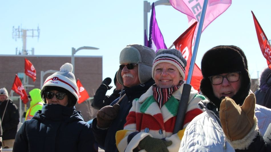 Four people dressed in warm coats and hats at a rally holing up flags