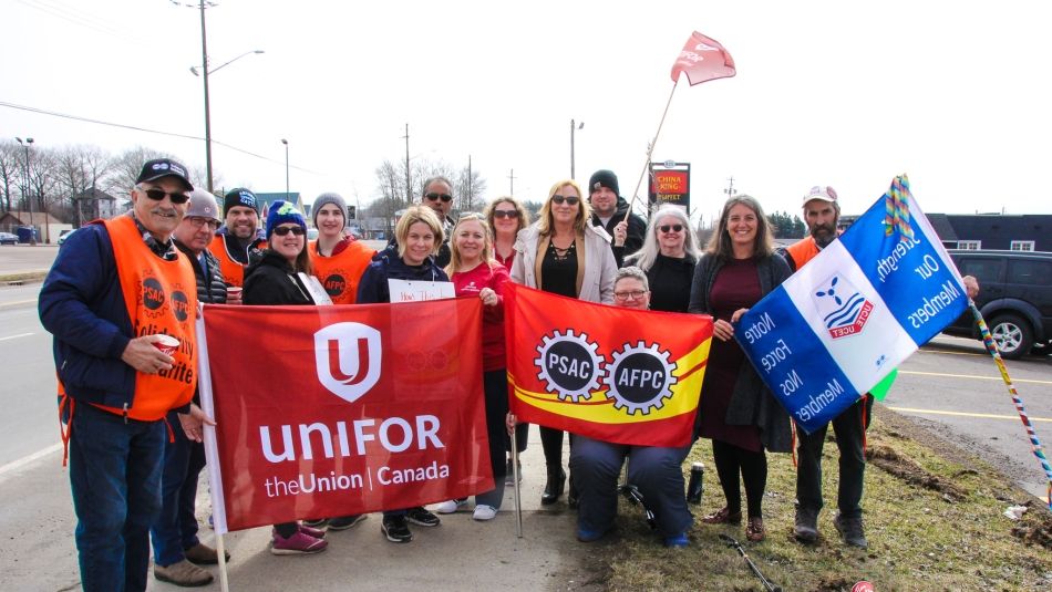 Unifor and PSAC members stand with flags on the picket line. 