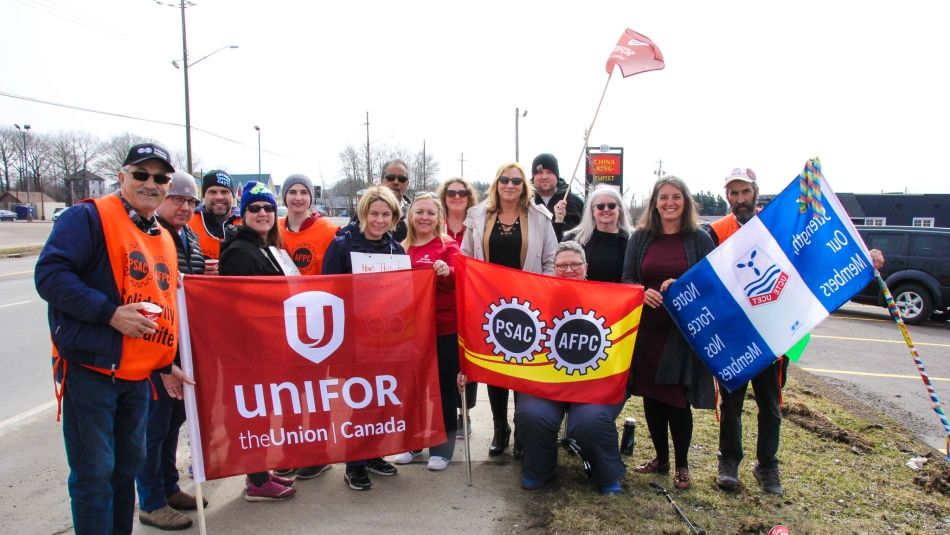 Unifor and PSAC members stand with flags on the picket line.