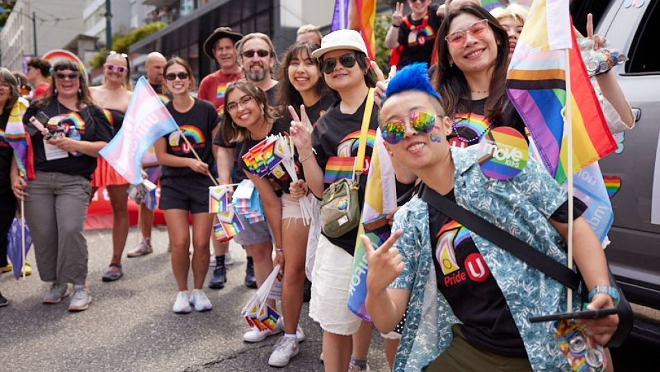 A large group of people outside wearing Unifor pride shirts and caring tans and pride flags