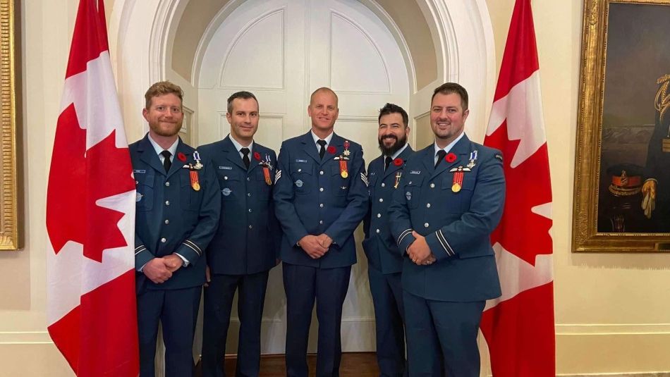 Cinq hommes debout entre deux drapeaux du Canada
