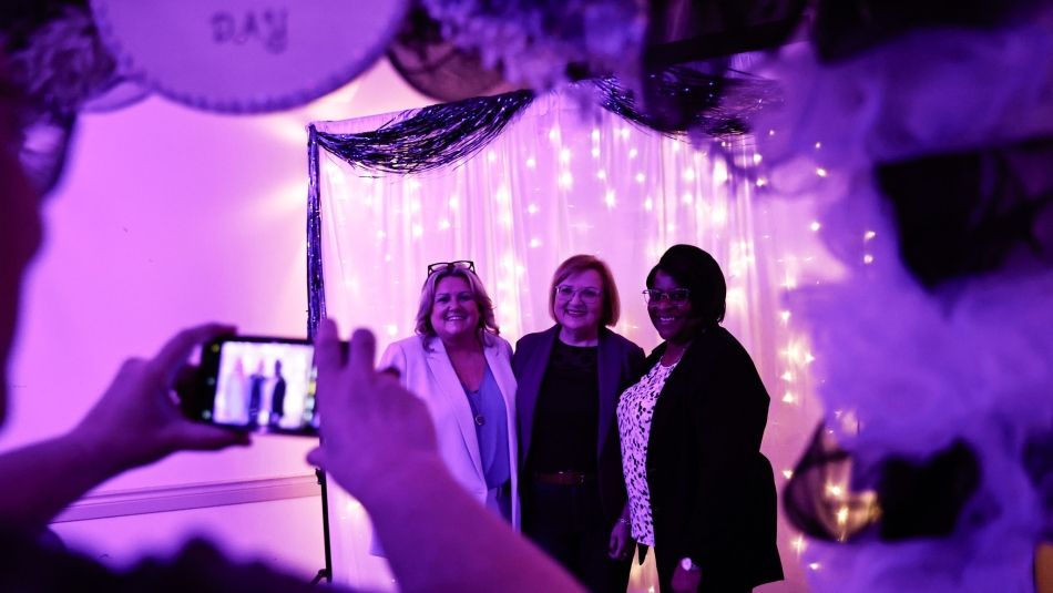 Unifor National President Lana Payne with two members standing under a balloon arch with someone taking a photo in the foreground.