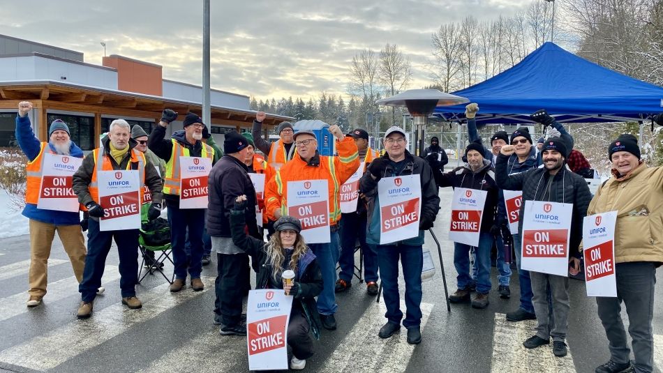 A group of people with their arms in the air with Unifor "On Strike" signs.