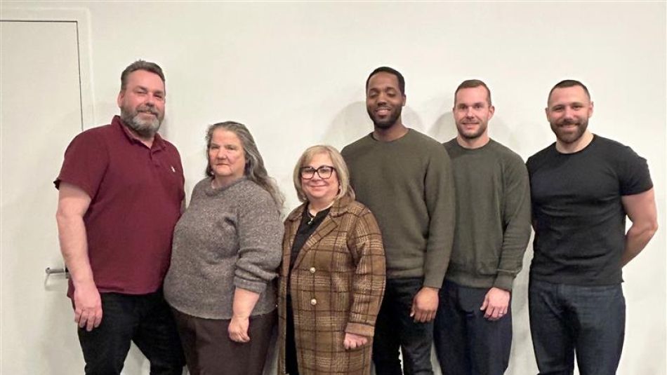 Six people posing in front of a beige wall