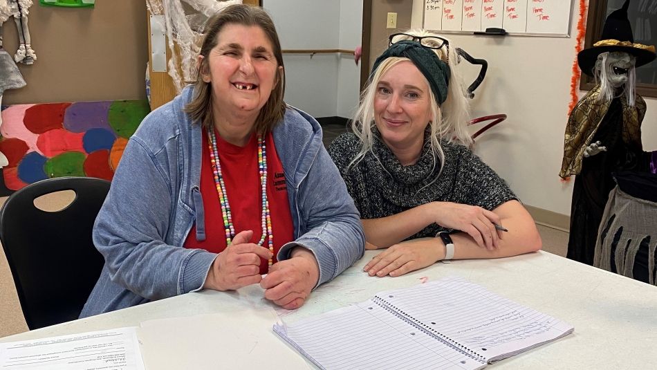 Two women sitting at a table in the community living centre smiling.