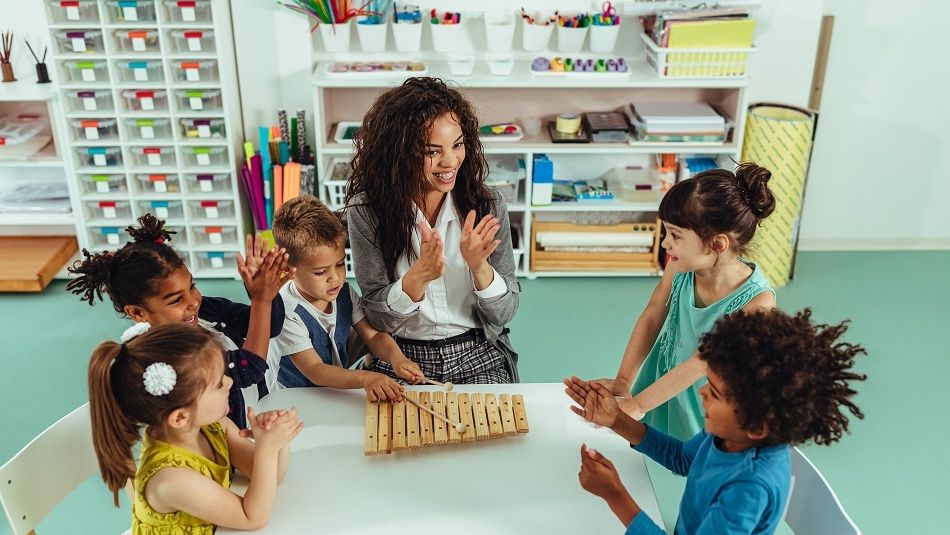 Children sitting with a teacher playing an xylophone