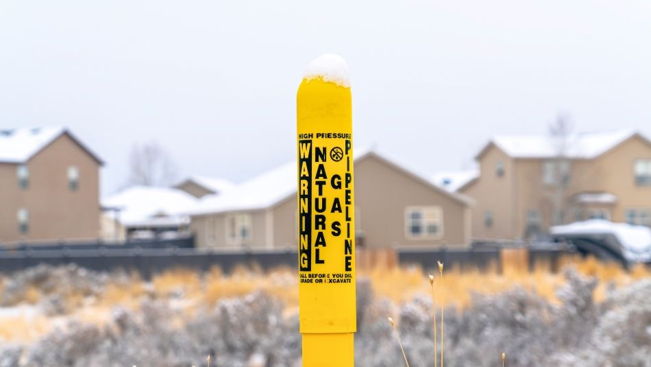 Gas line warning signage with subdivision of houses in the distance