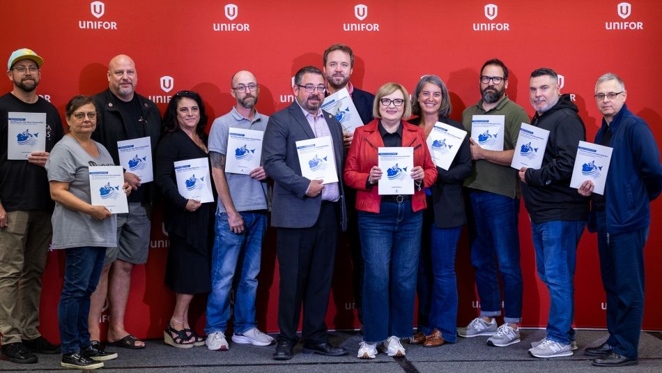 A large group holding up the new Aerospace policy document in front of a Unifor banner.