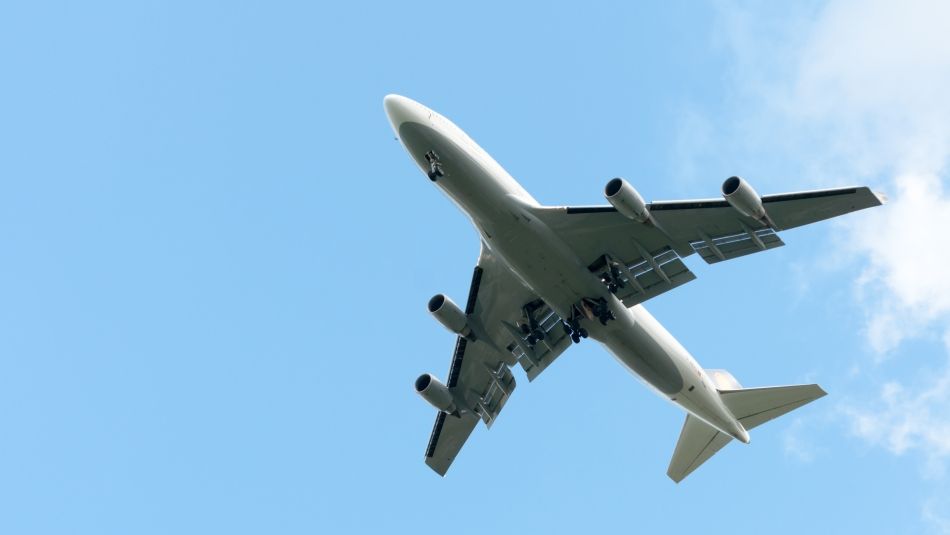 An airplane flying in a clear blue sky with little clouds.