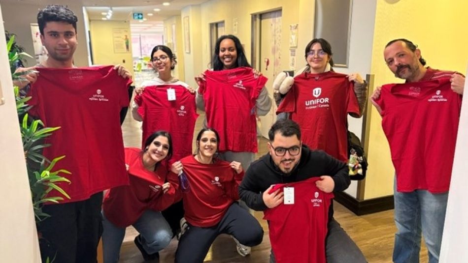 A small group of call centre workers hold up red Unifor t-shirts, smiling at the camera. 