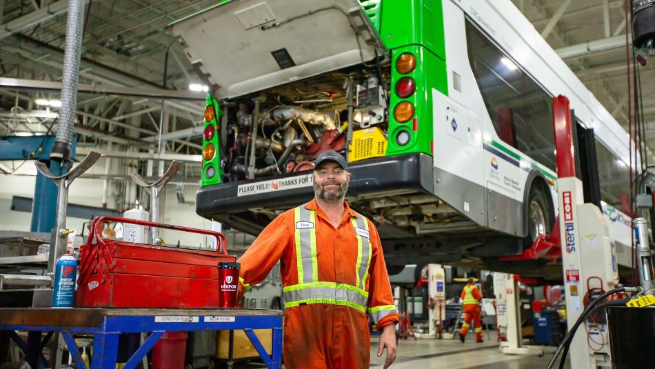 A man in orange and yellow coveralls in a bus factory 