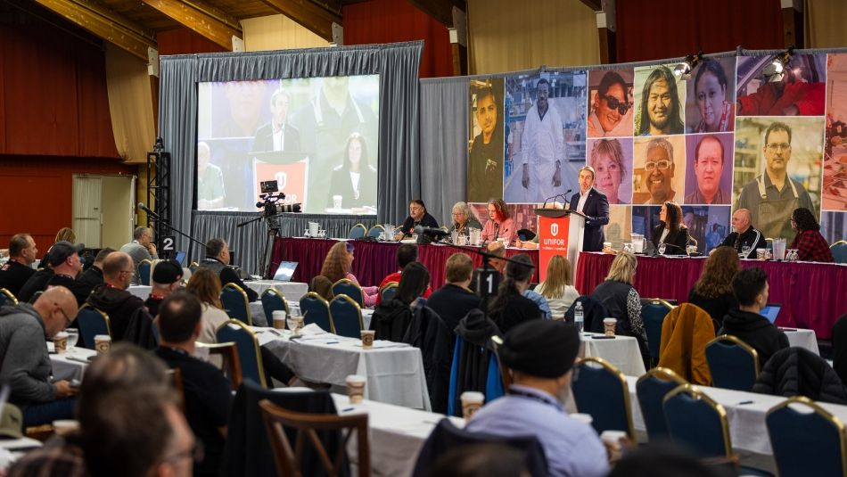 A large room with people seated classroom style and a person speaking from a podium.