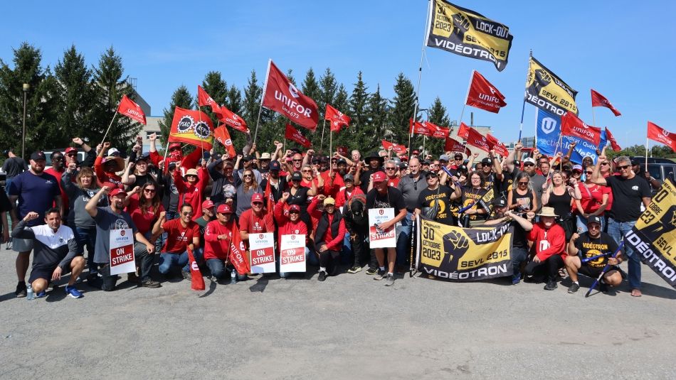 A group of people waving Unifor, PSAC and Videotron lockout flags