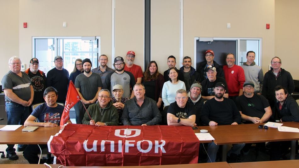A group of people behind a table with a red Unifor flag draped at the front.
