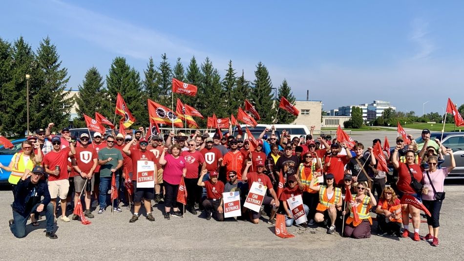 A group of people wearing red Unifor shirts holding flags.