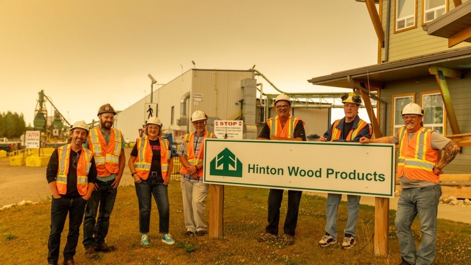 • A group of people wearing safety vests and standing in front of a sign at Hinton Wood Products.