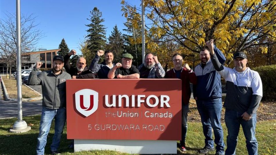 Les membres du comité de négociation des techniciennes et techniciens à Bell posent à côté de l’enseigne d’Unifor lors d’une pause dans les négociations.