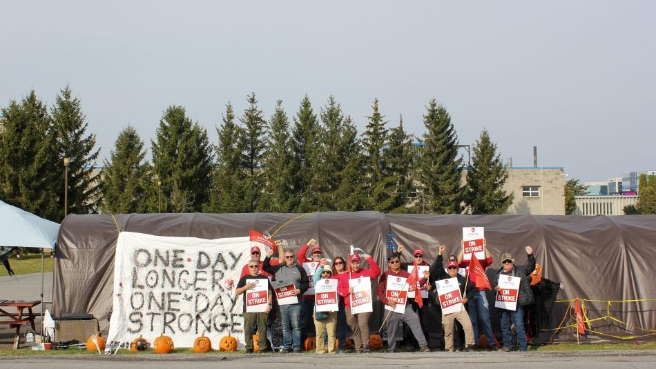 Striking Unifor Local 1541 members stand with fists raised outside their workplace. 