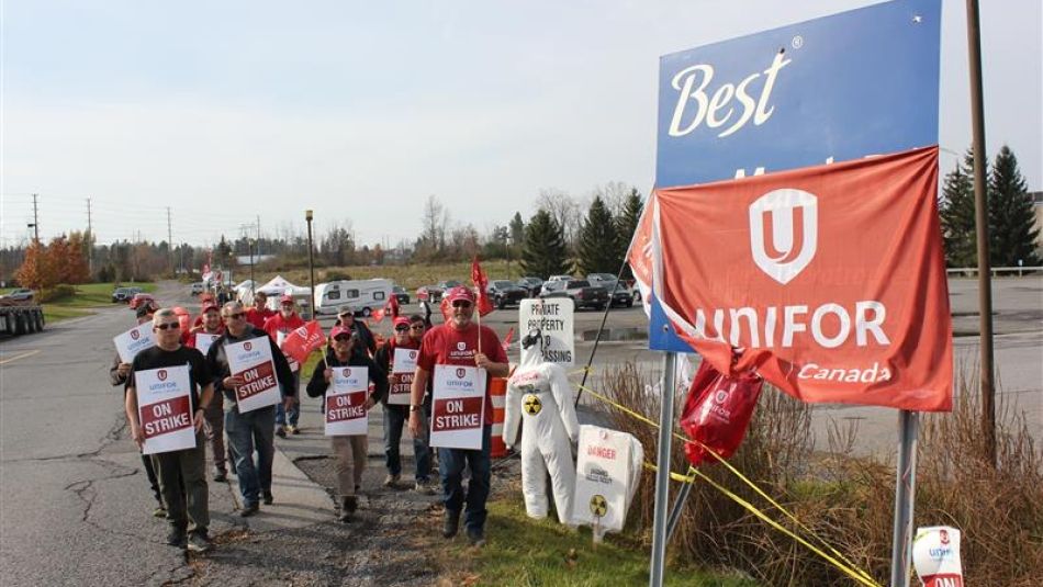 People on a picket line holing red Unifor flags and placcards