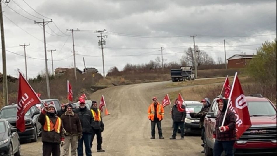 Des hommes portant des drapeaux d'Unifor et portant des gilets de chantier se tiennent sur un chemin de terre, avec un camion-benne en arrière-plan