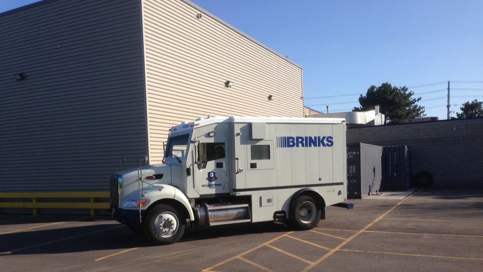 Brinks armoured truck parked outside a warehouse and loading area on a clear day
