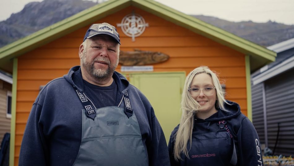 A man and women wearing coveralls in front of a orange fishing shead