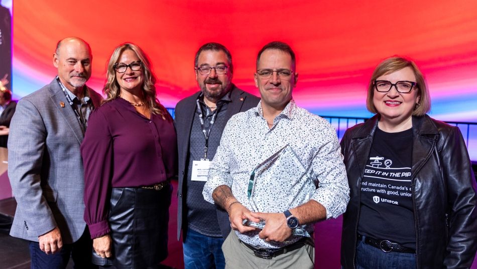Five people standing on stage one is holding an award.