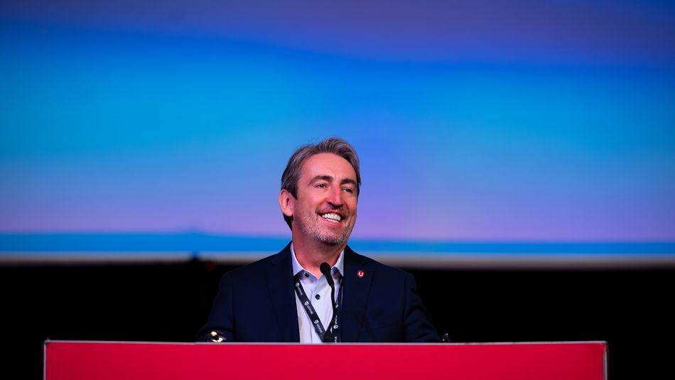 A man smiles and stands at a red podium.