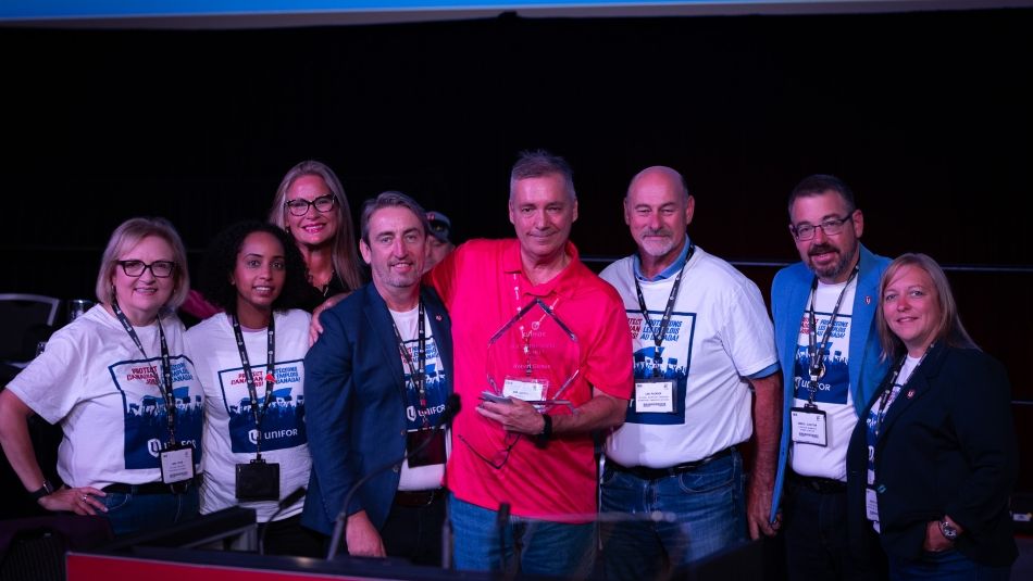 A large group on a stage one man holding a glass award