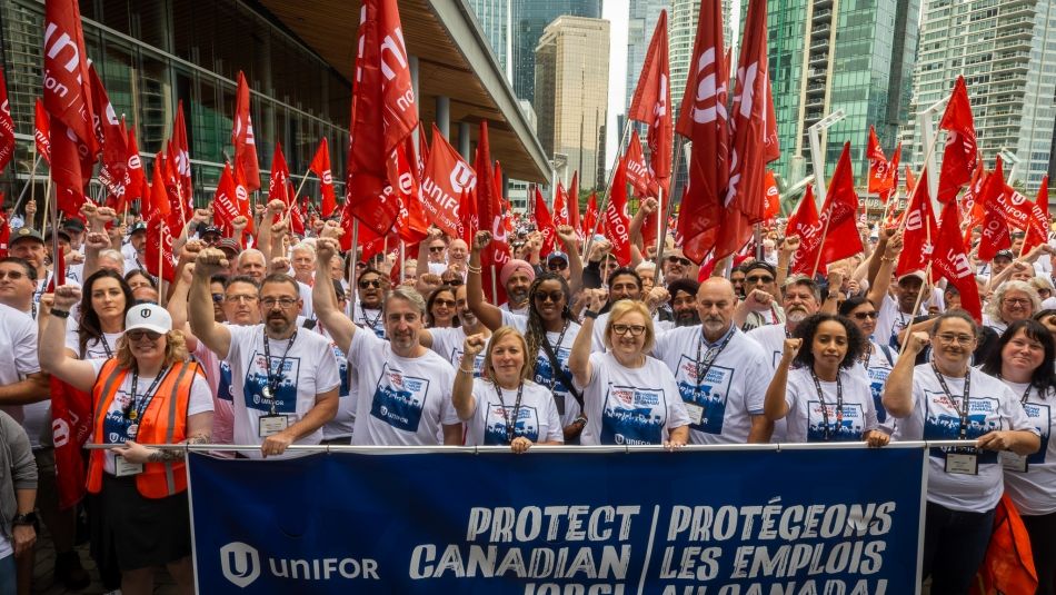 A huge rally standing behind a Unifor "Protect Jobs Banner" a sea of red Unifor flags