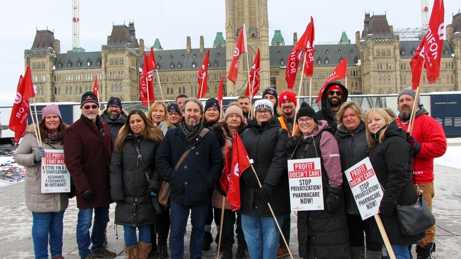 A group of people holding red Unifor flags and signs in front of Parliament Hill.