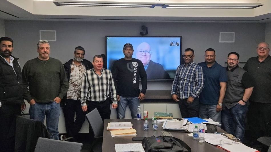 Nine men standing in front of a boardroom presentation screen