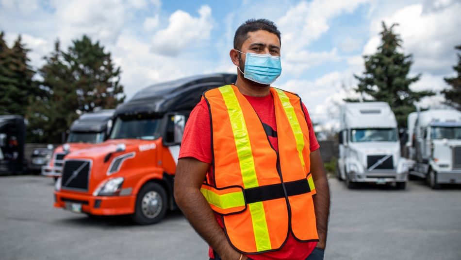 Homme en gilet de sécurité et masque facial debout devant un camion