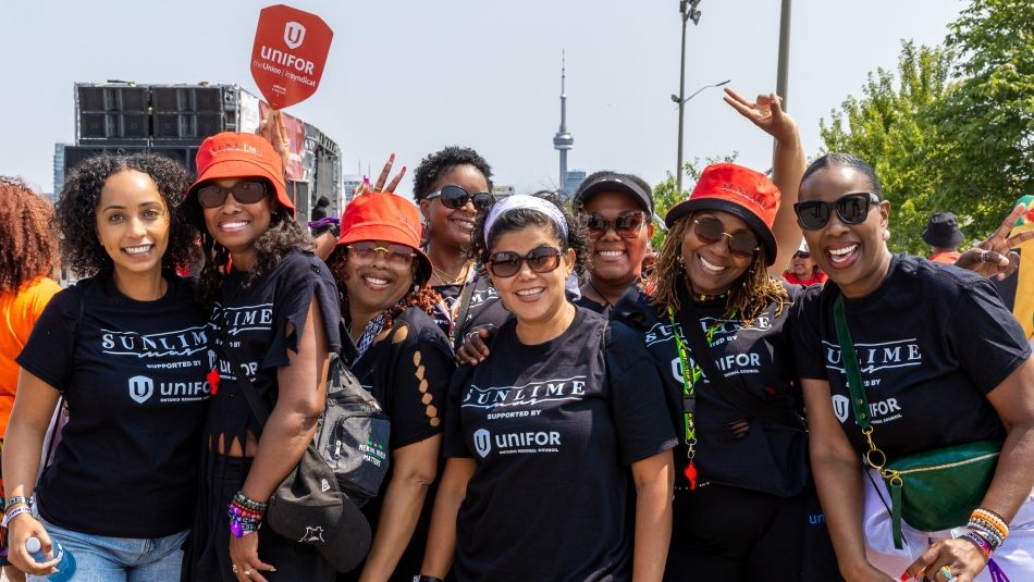 Eight people outside wearing black Unifor t-shirts smiling and having fun at Caribbean Carnival